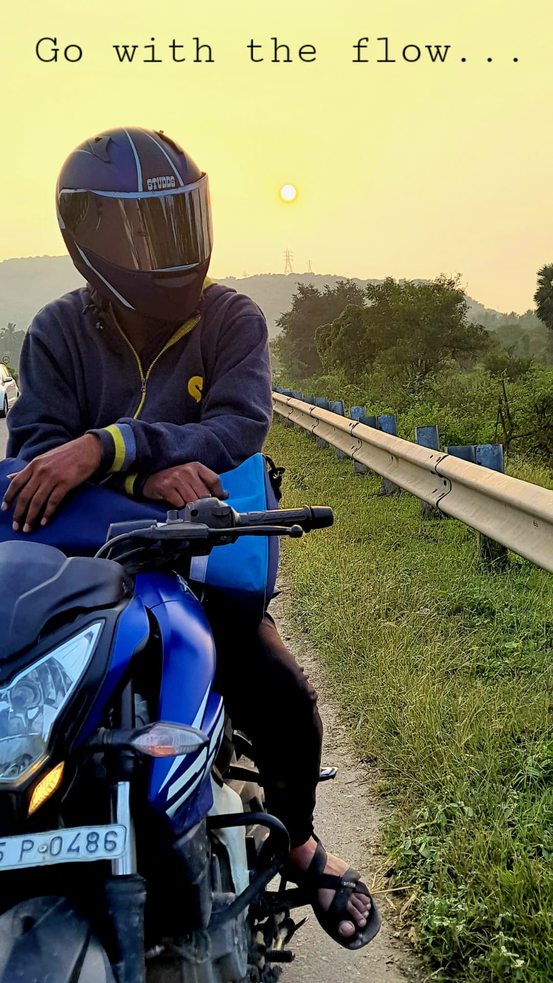 Motorcycle rider stopped beside a green roadside landscape at sunset